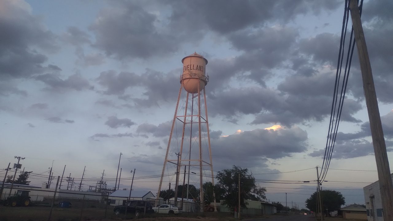 The Levelland water tower rising above a street and utility lines under heavy evening clouds.